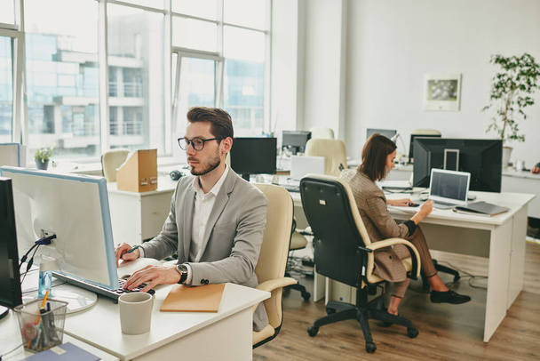 Kaksi liikemiestä istuu toimistopöydillä ja käyttää tietokoneita, kun taas heidän kollegansa työskentelevät kotoa sepelvaltimoviruksen eristämisen aikana. - Valokuva, kuva
