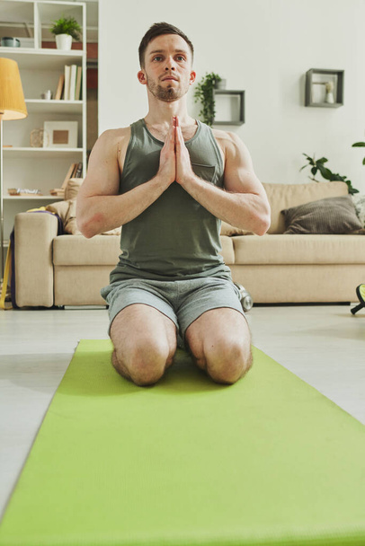 Entspannter Mann in Aktivkleidung, die Hände eng an der Brust zusammengelegt, auf Knien stehend, während er eine der Yoga-Übungen praktiziert - Foto, Bild
