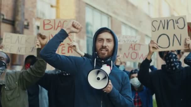 Jeune homme blanc beau gars protestant au milieu de la foule multiethnique de manifestants et criant des slogans en mégaphone. Un homme qui mène une manifestation pour les droits humains. - Séquence, vidéo