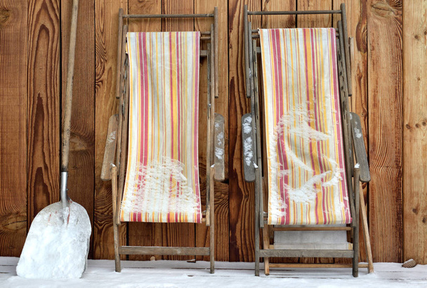 ligstoelen gevouwen en geplaatst tegen een houten muur op een terras bedekt met sneeuw  - Foto, afbeelding