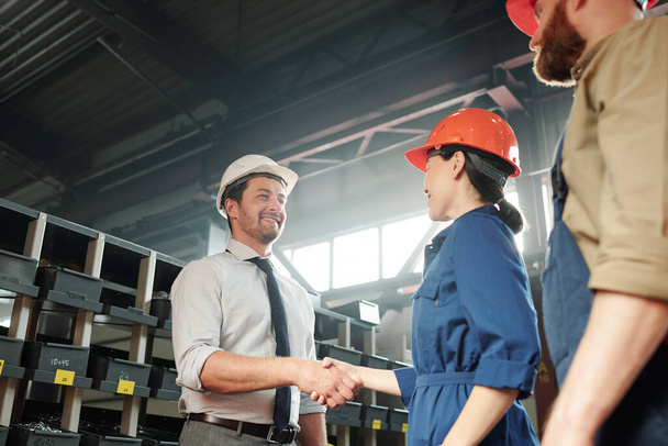 Позитивный привлекательный бизнесмен в рукопожатии с инженером-заводчиком в современном цехе промышленного завода
 - Фото, изображение