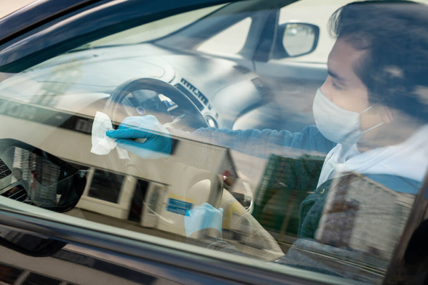 Handschuhjunger Mann in Maske reinigt Lenker mit feuchtem antiseptischem Tuch, während er nach dem Einkaufen oder dem Besuch öffentlicher Plätze im Auto sitzt - Foto, Bild