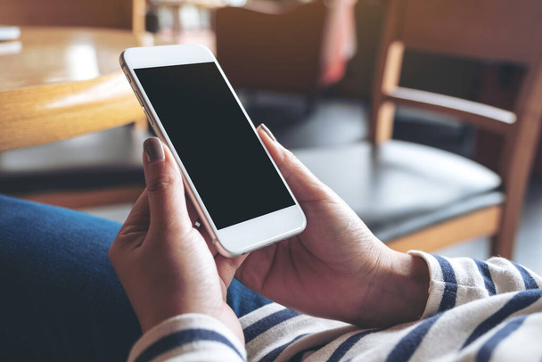 Wizerunek dłoni trzymających biały telefon komórkowy z czarnym ekranem w drewnianej kawiarni - Zdjęcie, obraz