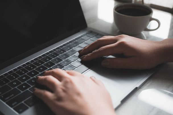 Imagen de cerca de las manos de una mujer usando y escribiendo en el teclado del ordenador portátil con taza de café en la mesa
 - Foto, imagen