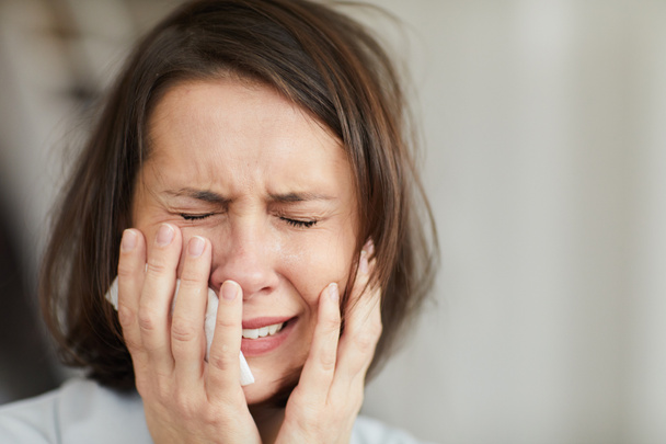 Close up portrait of disheveled adult woman crying hysterically with eyes closed and holding tissue, copy space - Photo, Image