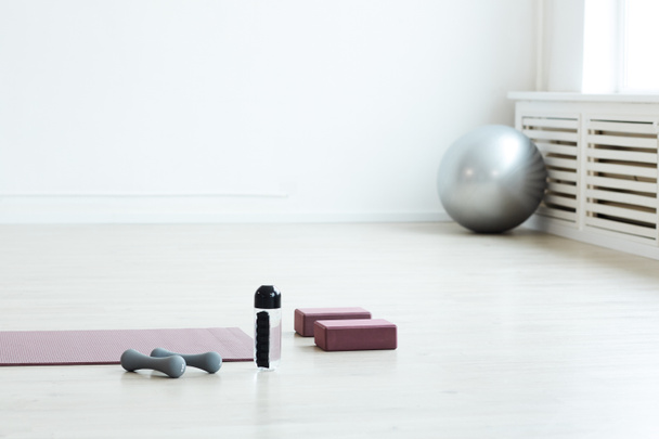 Minimális háttér kép a jóga szőnyegről és a sporteszközökről a padlón, üres fehér szobában, másolás - Fotó, kép