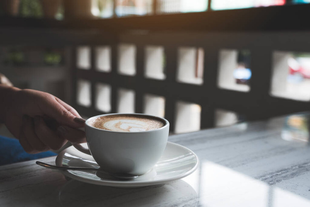 Image rapprochée des mains de la femme tenant une tasse de café chaud avec latte art coeur sur la table dans le café - Photo, image