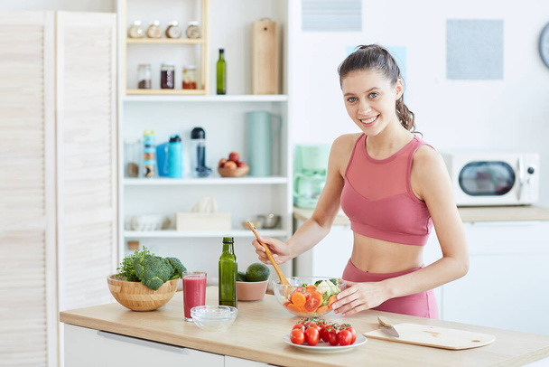 Retrato de cintura hacia arriba de la mujer joven en forma cocinando comida fitness en el interior de la cocina y sonriendo a la cámara, espacio para copiar
 - Foto, imagen