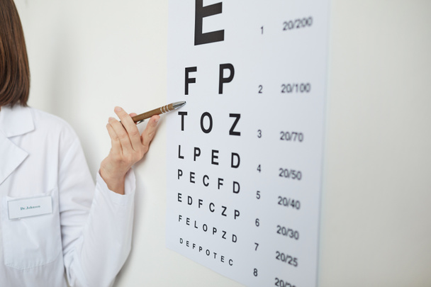 眼科クリニックでの視力検査中にラテン文字で目のチャートを指している女性の手のクローズアップ,コピースペース - 写真・画像