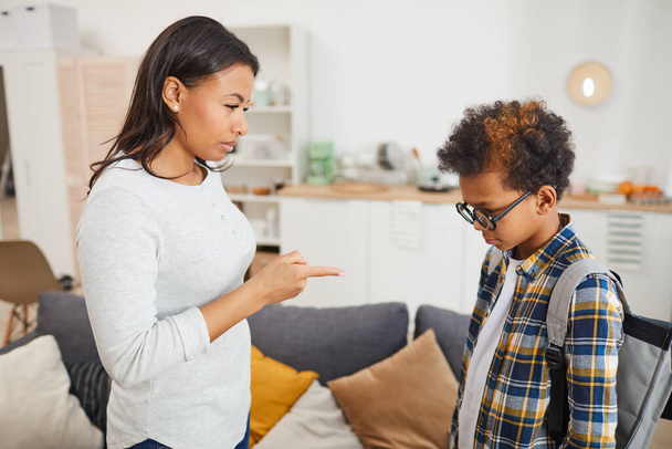 Side view portrait of young African-American woman scolding son for failing in school while standing in modern apartment interior - Photo, image