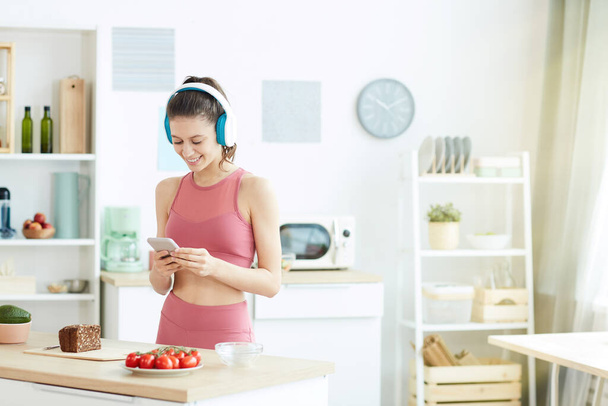 Талия портрет улыбающейся молодой женщины, слушающей музыку во время подготовки фитнес-обед в кухонном интерьере, скопировать пространство
 - Фото, изображение