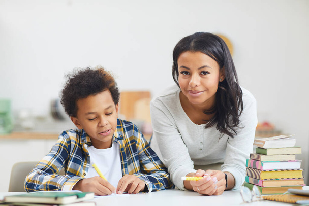 Portrait of young African-American woman smiling at camera while helping son studying at home, copy space - Photo, image