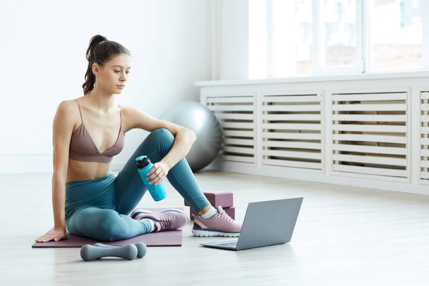 Minimális teljes hosszúságú portré fitt fiatal nő nézi sport videók laptopon otthoni edzés során fehér szobában, másolás hely - Fotó, kép