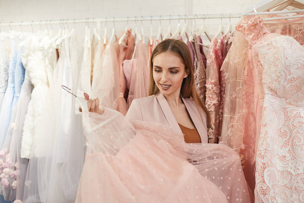 Waist up portrait of beautiful woman choosing feminine dress while standing against clothing racks in shop, copy space - Φωτογραφία, εικόνα