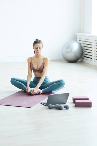 Minimale volledige lengte portret van fit jonge vrouw opwarmen en stretching tijdens het bekijken van workout video via laptop thuis, kopiëren ruimte - Foto, afbeelding