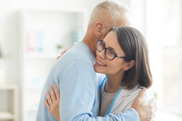 Ritratto in vita di un giovane medico donna che abbraccia un paziente anziano grato e sorride felicemente mentre è in carica, copia lo spazio - Foto, immagini