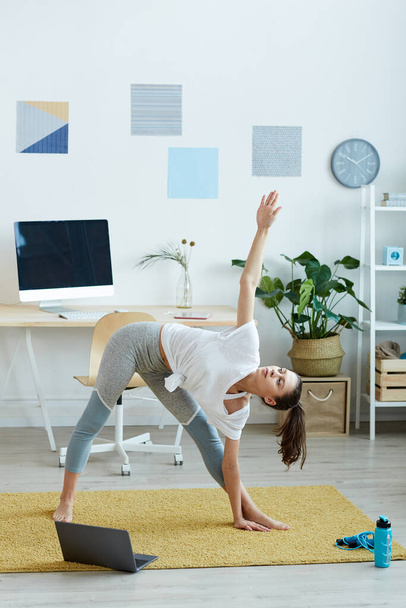 Retrato vertical de comprimento total da jovem contemporânea fazendo exercícios de ioga durante o treino de fitness em casa, espaço de cópia
 - Foto, Imagem