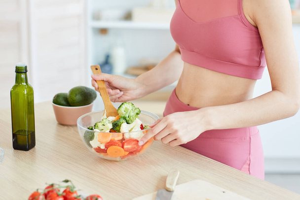 Primer plano de mujer deportiva irreconocible revolviendo ensalada en un tazón mientras cocina alimentos saludables, copiar espacio
 - Foto, imagen