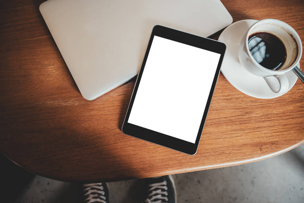 Верхний вид макет изображения черного планшета ПК с чистым рабочим столом белый экран с ноутбуком и чашкой кофе на деревянном столе
 - Фото, изображение