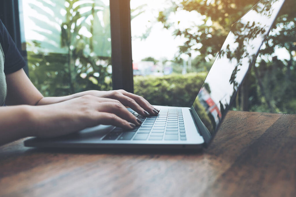 Szoros kép a női kéz dolgozik és gépelés laptop billentyűzet fa asztal zöld természet háttér - Fotó, kép