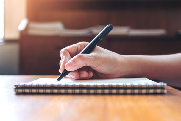 Imagem de close-up de uma mão escrevendo em um caderno em branco branco na mesa de madeira
  - Foto, Imagem