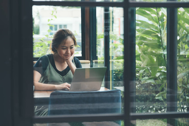 Immagine primo piano di una donna d'affari asiatica che lavora e utilizza laptop su tavolo in legno in ufficio con sfondo verde natura
 - Foto, immagini