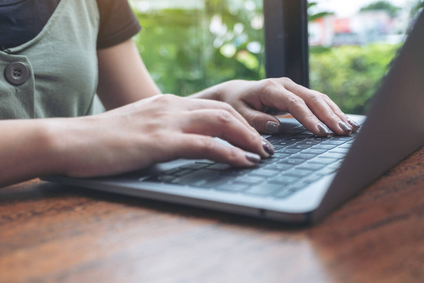 Immagine ravvicinata delle mani di una donna d'affari che lavora e digita sulla tastiera del computer portatile su un tavolo di legno con sfondo verde
 - Foto, immagini