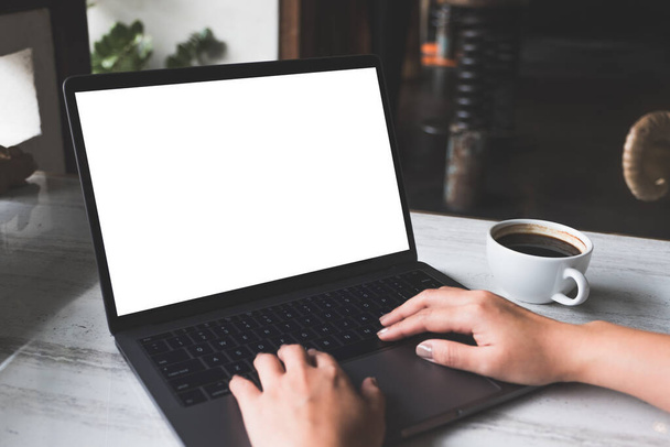 Mockup kép egy nő használ és gépel a laptop üres fehér képernyő és kávéscsésze az asztalon a modern kávézó - Fotó, kép