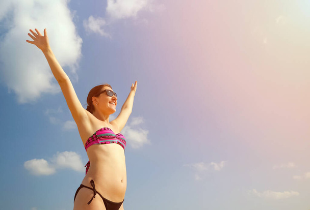 Happy girl in bikini stands raising arms up - Фото, изображение