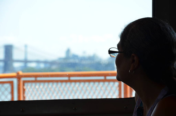 Frau mit Ohrring blickt aus Fenster der Fähre auf Wasser in New York - Foto, Bild