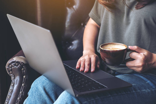 Closeup image of a woman working and typing on laptop keyboard while drinking coffee - Photo, Image
