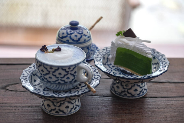 Uma xícara de leite quente com um pedaço de bolo em um antigo tailandês tradicional benjarong estilo recipientes
 - Foto, Imagem
