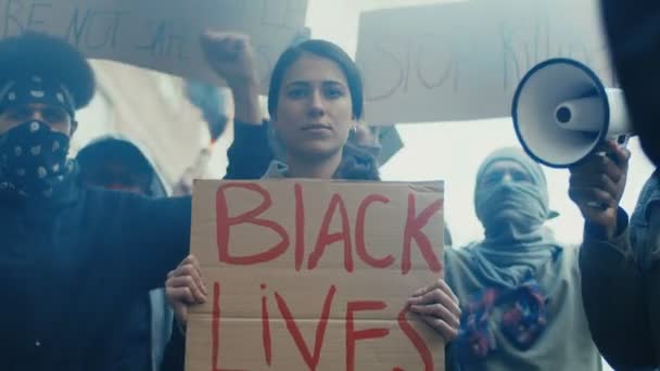 Молодая белая красивая женщина, стоящая в кричащей толпе с плакатом "Жизнь чернокожих важна". США протестуют против расизма и полицейского насилия. Девушка на демонстрации за равенство
. - Кадры, видео
