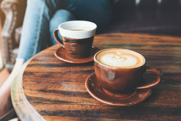 Closeup image of two cups of hot latte coffee and black coffee on vintage wooden table in cafe - Foto, Imagem