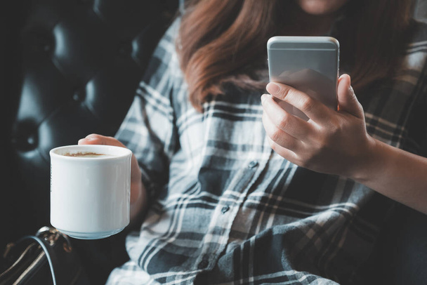 Immagine ravvicinata di una donna che tiene in mano, utilizza e tocca uno smartphone mentre beve caffè
 - Foto, immagini