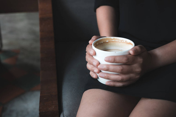 Imagen de cerca de una mujer sosteniendo una taza de café caliente mientras está sentada en la cafetería
 - Foto, Imagen