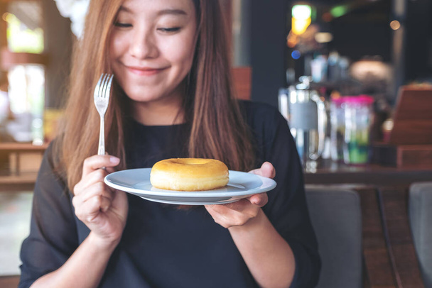 Uma bela mulher asiática segurando um pedaço de donut e garfo com sentir-se feliz no café
 - Foto, Imagem