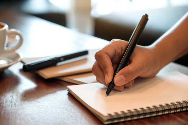 Imagen de primer plano de una mano escribiendo en un cuaderno blanco en blanco con taza de café en la mesa de madera
 - Foto, imagen