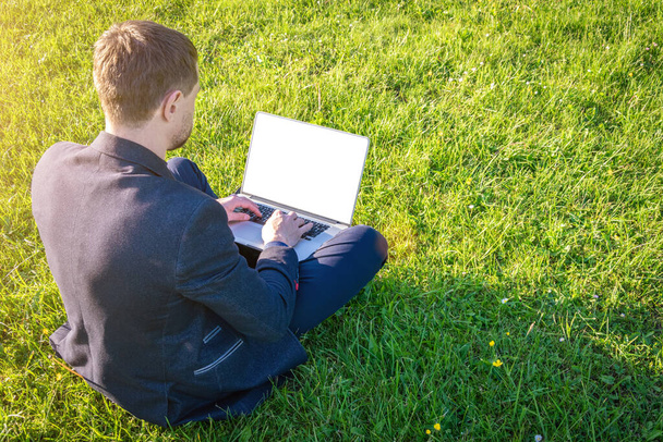 Työasioita ulkona. Opiskelijapoika työskentelee kannettavan tietokoneen kanssa, tietokone tabletti kesäpuistossa. Online-teknologia ihmisen kanssa ulkona. Pakeni toimistoetäopetuskonseptista. Matkijat - Valokuva, kuva