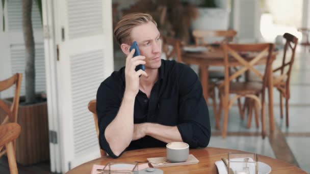 Portrét pohledného muže pije kávu v moderní kavárně a mluví po telefonu - Záběry, video