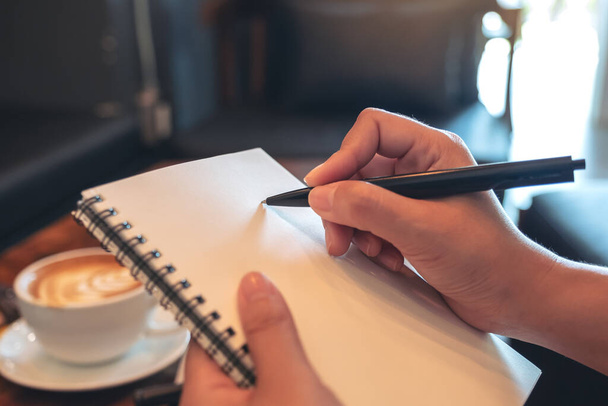 Image rapprochée des mains d'une femme tenant et écrivant sur un carnet blanc vierge dans un café - Photo, image