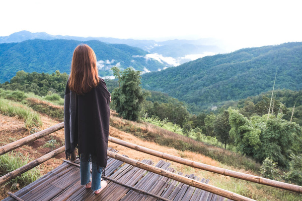 Een vrouw die alleen staat en kijkt naar bergen op mistige dag met blauwe lucht achtergrond in de ochtend - Foto, afbeelding