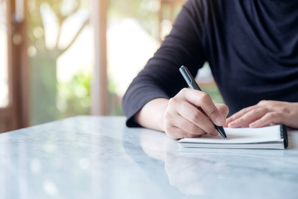 Closeup image of a woman writing on blank notebook on table with green nature background - Foto, afbeelding