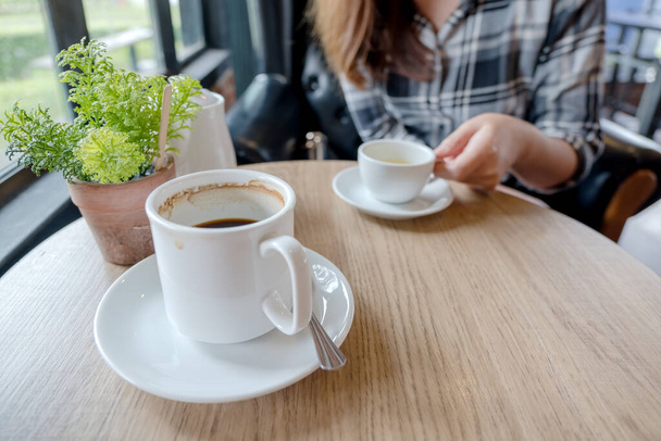 Крупним планом зображення жінки, що тримає білу чашку гарячого чаю з чашкою кави на дерев'яному столі в кафе
 - Фото, зображення