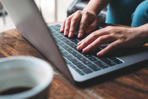 Imagen de cerca de las manos de una mujer trabajando y escribiendo en el teclado del ordenador portátil con la taza de café en la mesa de madera
  - Foto, Imagen