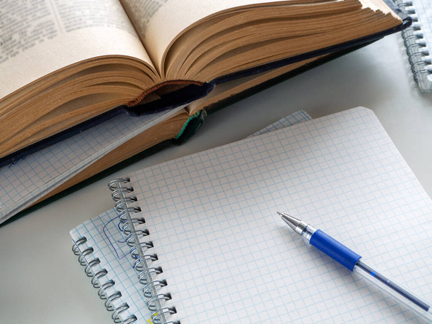 Ανοιχτά βιβλία και σημειωματάρια είναι στο τραπέζι. Ένα στυλό βρίσκεται σε ένα κενό φύλλο ενός σημειωματάριου. Ιστορικό εκπαίδευσης, επιστημονικών εργασιών, βιβλιοθηκών. - Φωτογραφία, εικόνα