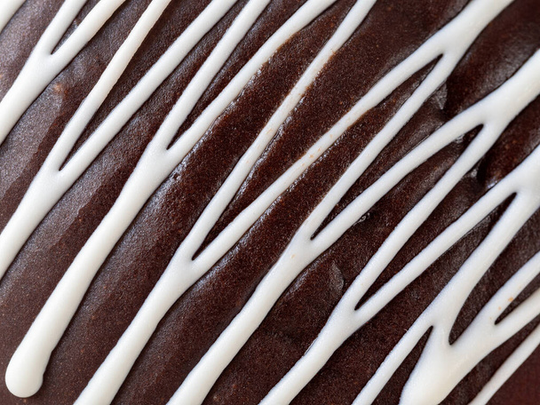 Süßer Hintergrund mit Schokoladenglasur. Ein Zickzack wird auf Schokolade mit weißem Zuckerguss aufgetragen. Hintergrund und Struktur der Tortenoberfläche. - Foto, Bild