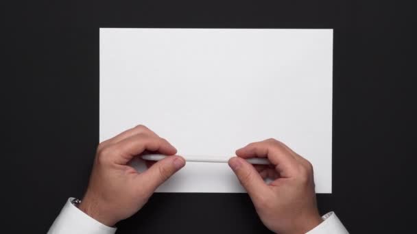 vista superior de una hoja de papel en blanco y las manos de un hombre de negocios sobre una mesa negra, camisa blanca y reloj de pulsera
 - Metraje, vídeo