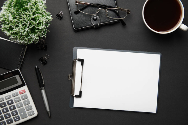 Top view of modern black office desk with blank paper sheet, notebook, pen and a lot of things. Flat lay table layout. Copy space for text. - Photo, Image