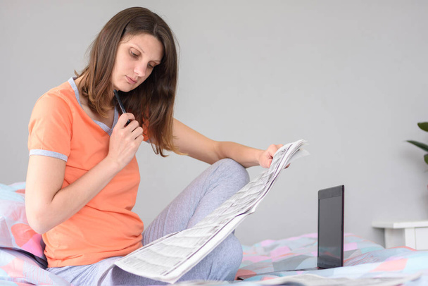 Una chica está buscando trabajo mirando a través de anuncios en el periódico, al lado de una computadora portátil
 - Foto, imagen